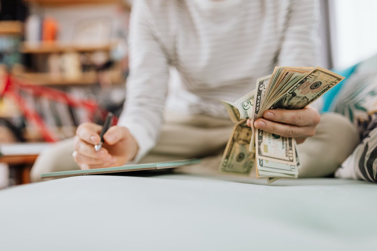 Individual counting money with pen in hand inside a cozy room setting.